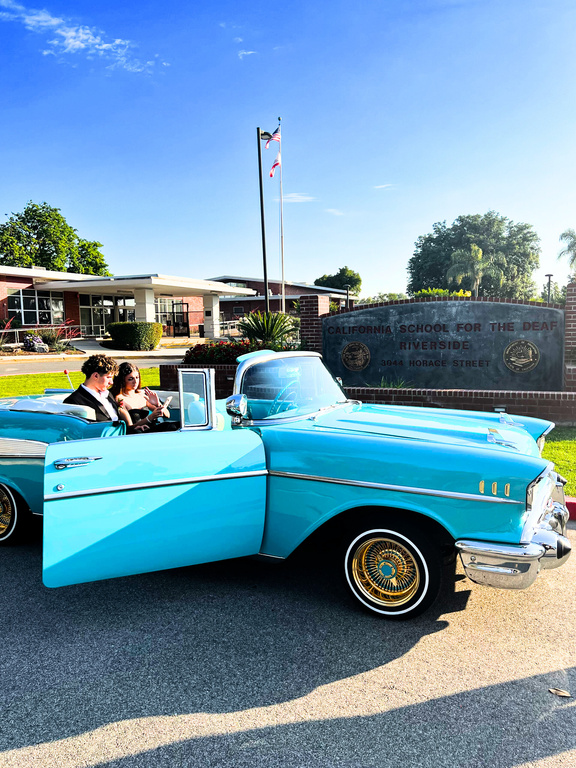 On Prom Night 2023, Senior Richard Silva leaves the CSDR campus with Sofia Giansanti in a bright blue ‘57 Chevrolet Bel Air classic, parked in front of the CSDR front sign by the brick Administration building